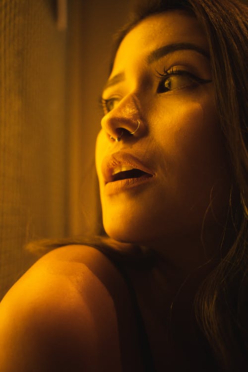 Woman taking a selfie under warm indoor lamp light — skin appears orange-tinted and face has harsh shadow on one side