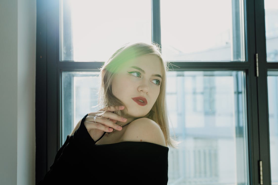 Woman taking a selfie facing a window with soft, even natural daylight — face is evenly lit with no harsh shadows
