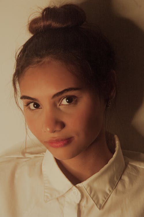 Woman in a plain white top with hair pulled back in a bun, face fully visible including jawline and neck